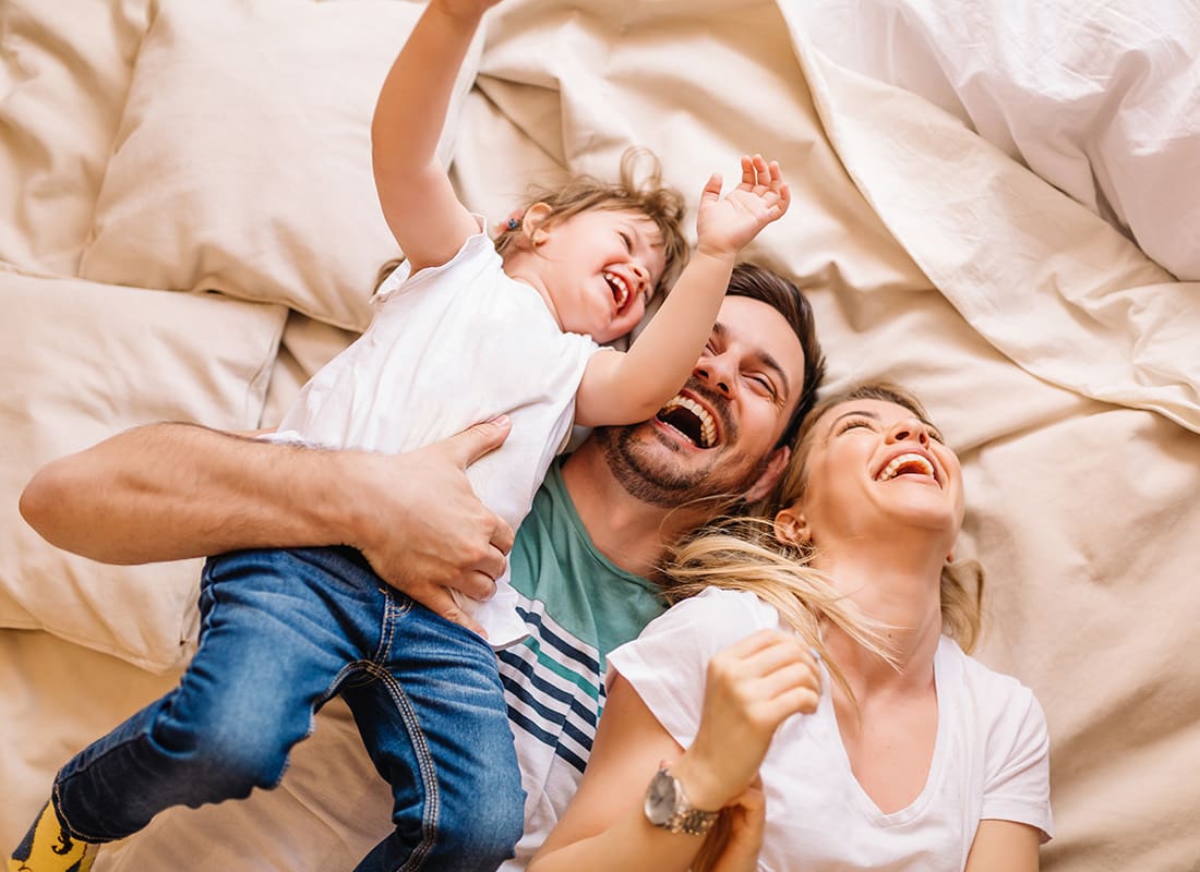 Personal Insurance - Portrait of a Cheerful Family Having Fun Laying in the Bed with Their Son